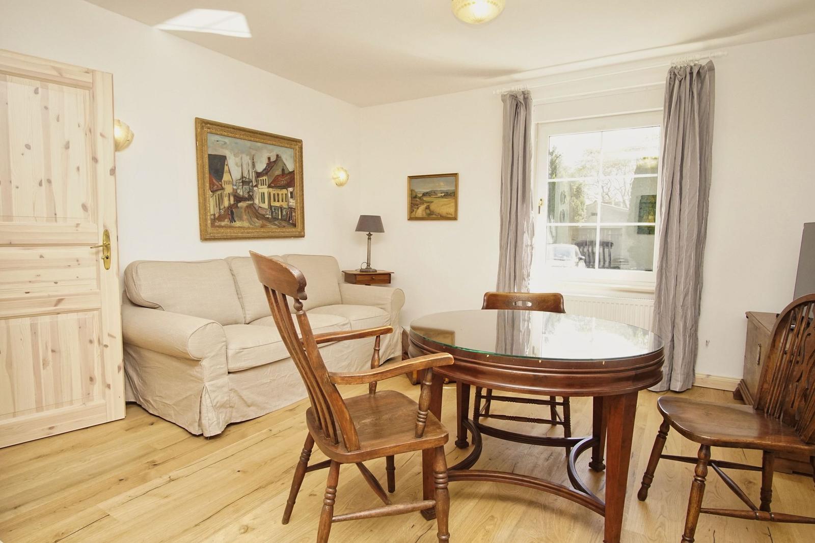 Wohn- und Essbereich mit Holzfußboden, Sofa, Esstisch und Stühlen sowie Fenster mit Vorhängen.