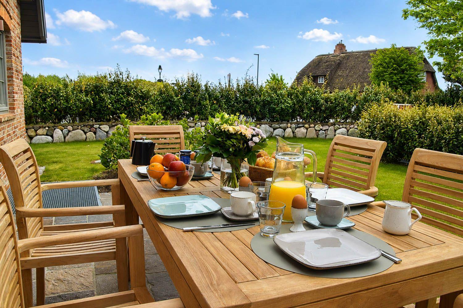 Holztisch mit Stühlen im Garten. Frühstückszubehör und Obst auf dem Tisch.