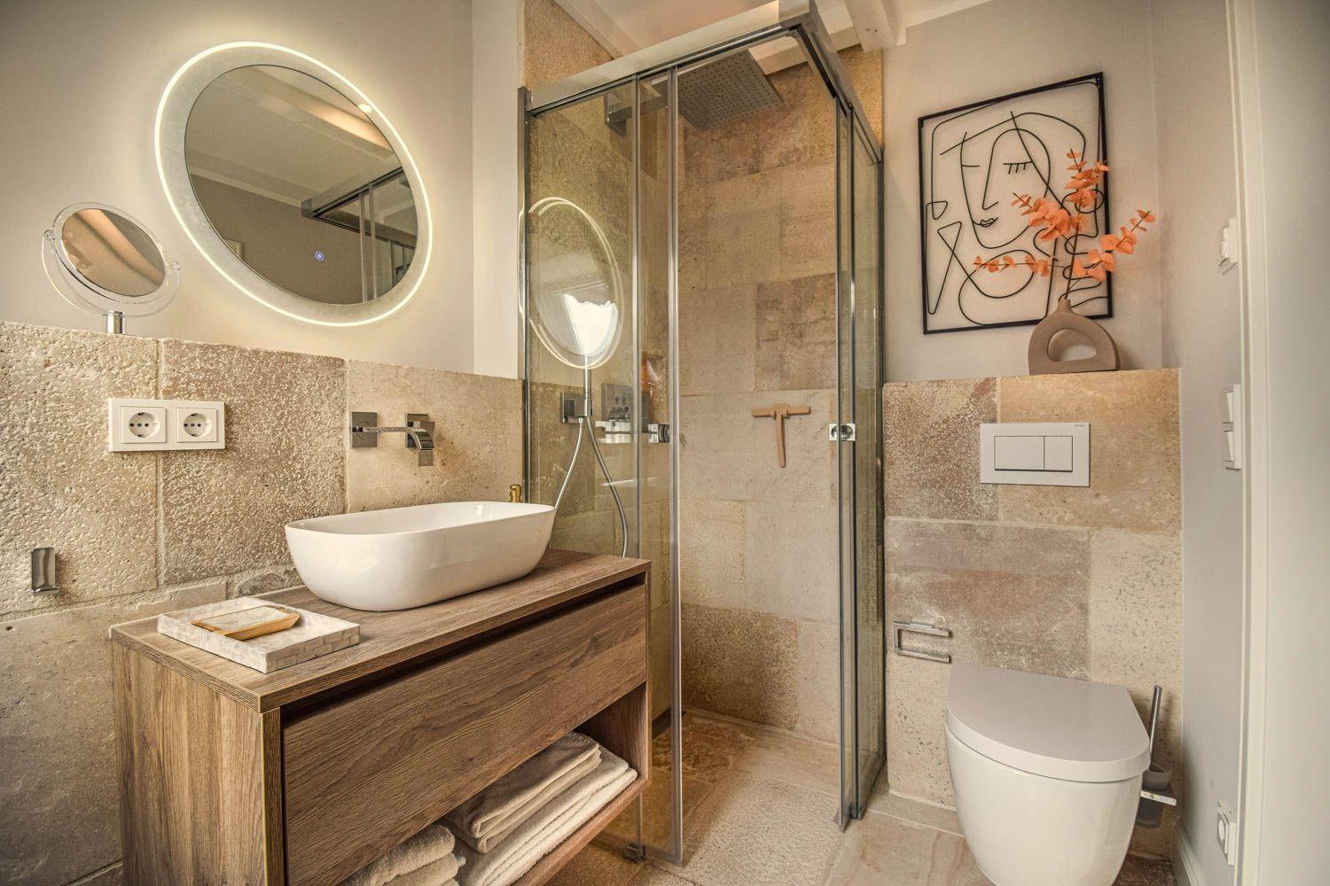 Badezimmer mit Dusche, Waschbecken und Toilette. Steinwand und Holzwaschtisch.