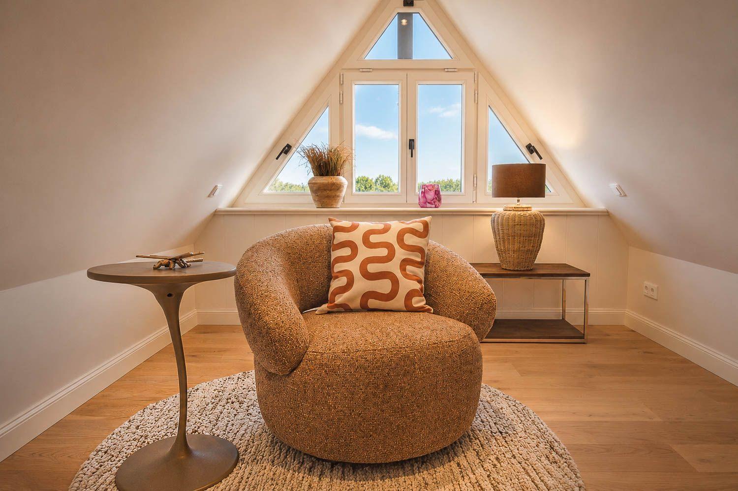 Eckzimmer mit Sessel, Tisch und Fenster mit Blick nach draußen.