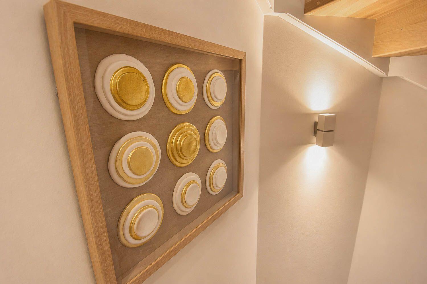 Wanddekoration mit goldenen Kreisen in Holzrahmen neben einer Wandlampe.