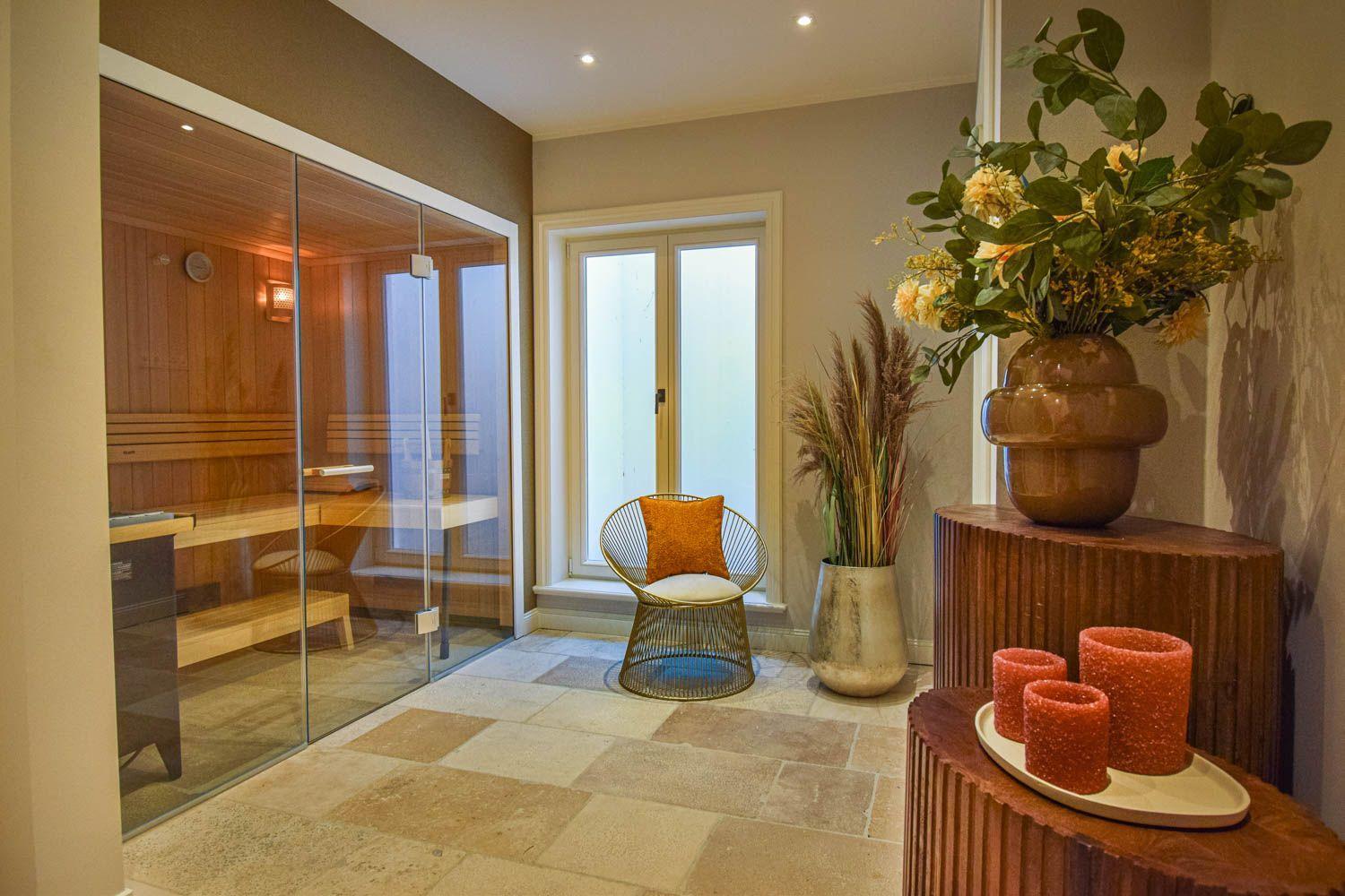 Sauna mit Glaswand, Sitzgelegenheit und Dekoration im Eingangsbereich.