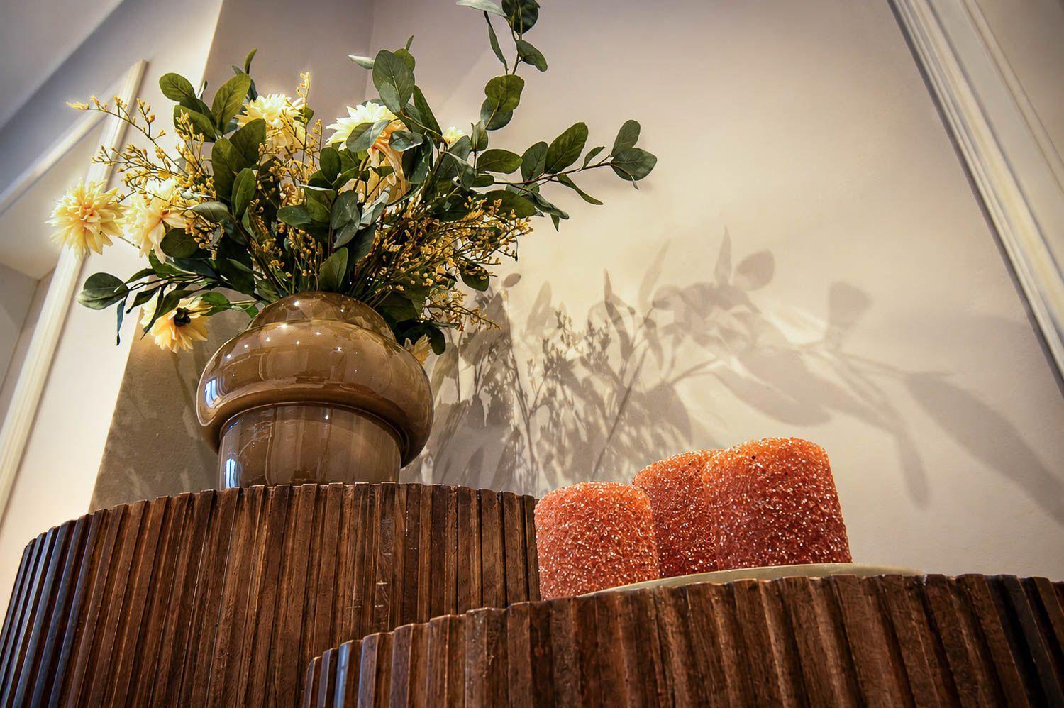 Ein brauner Vasenuntersatz mit Blumen und zwei orangefarbenen Kerzen auf einem Holztisch.