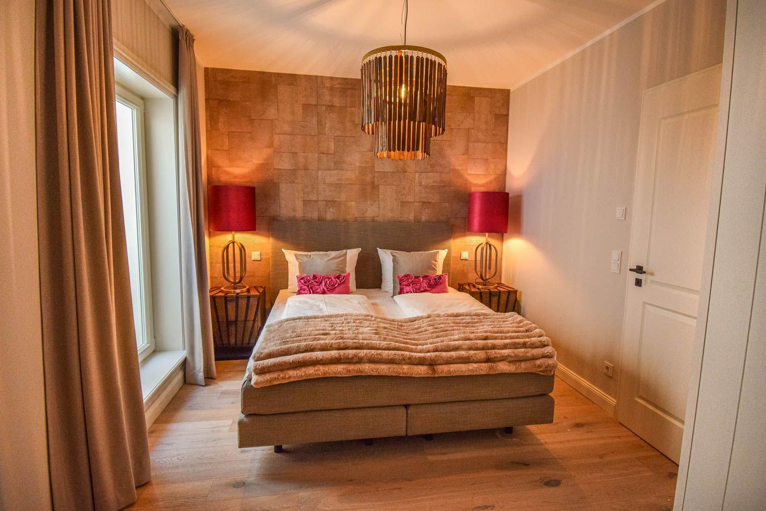 Schlafzimmer mit Bett, Nachttischen und Lampe. Holzboden und Fenster mit Vorhängen.