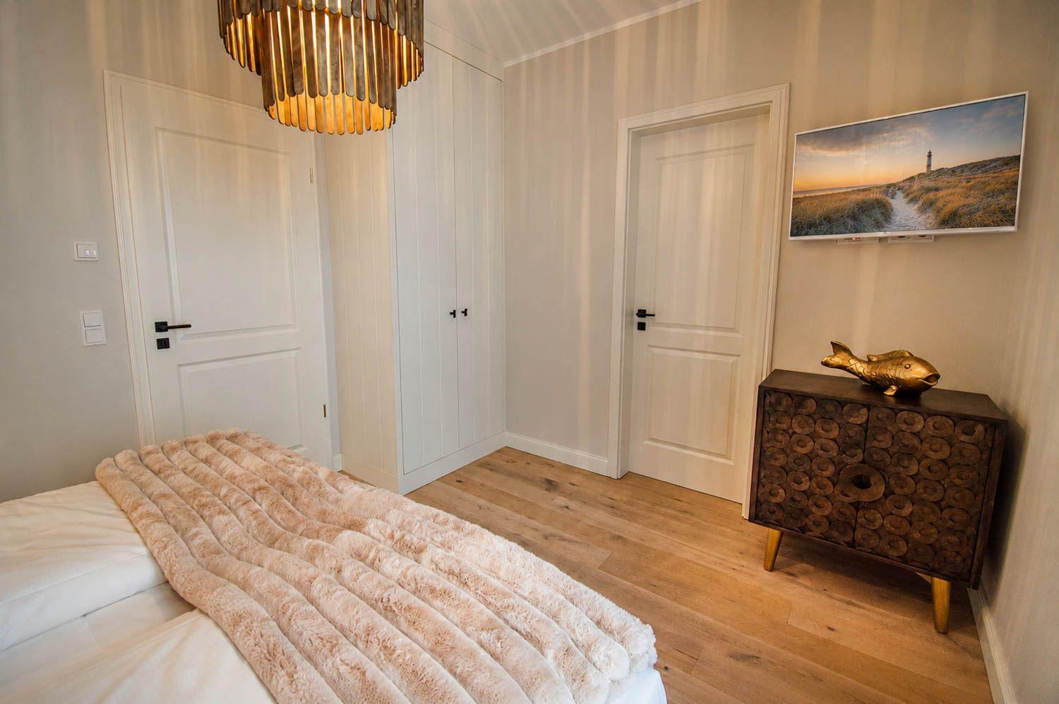 Schlafzimmer mit Bett, Holzboden, Schrank, Fernseher und goldener Fischfigur.