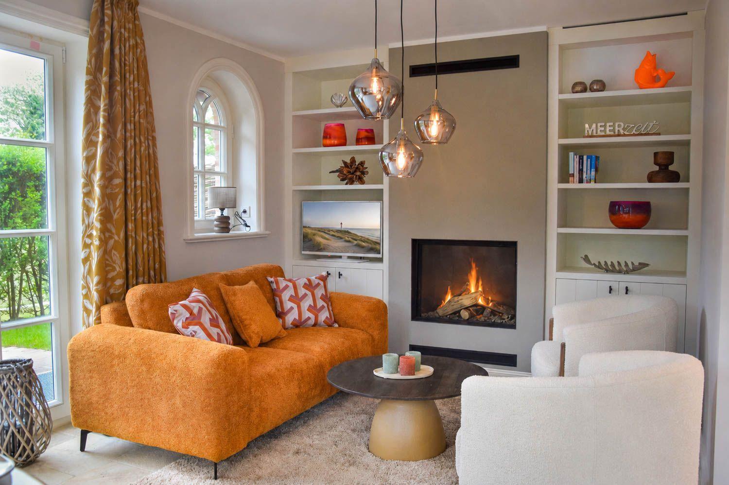 Ein Wohnzimmer mit orangefarbenem Sofa, Kamin und weißen Sesseln.