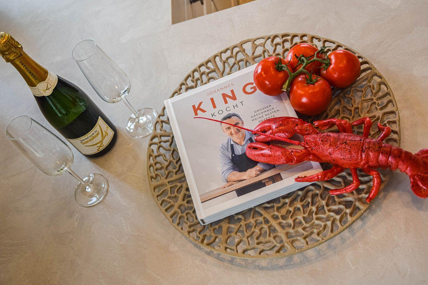 Ein Buch, eine Garnel und Tomaten auf einem Teller mit Champagnergläsern.