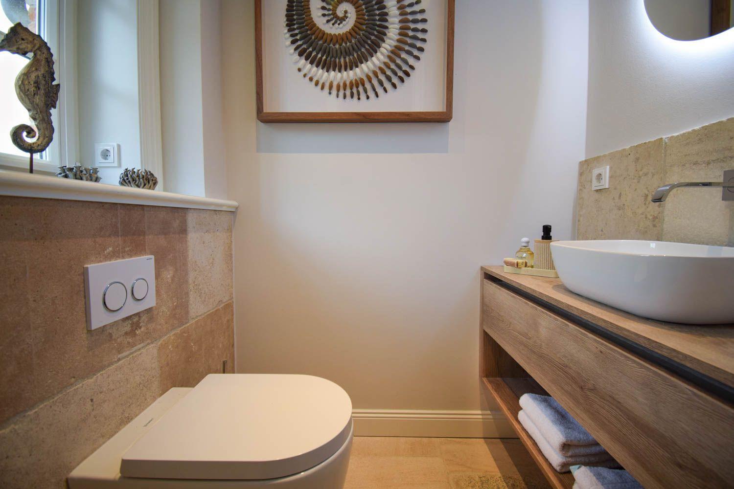 Badezimmer mit Toilette, Waschbecken und Wandbild aus Steinen.