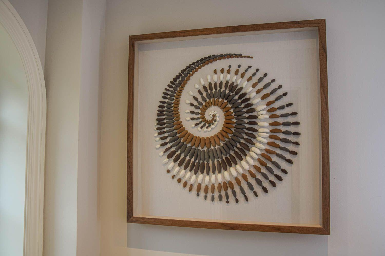 Wanddekoration aus Steinen in Form einer Spirale in einem Holzrahmen.