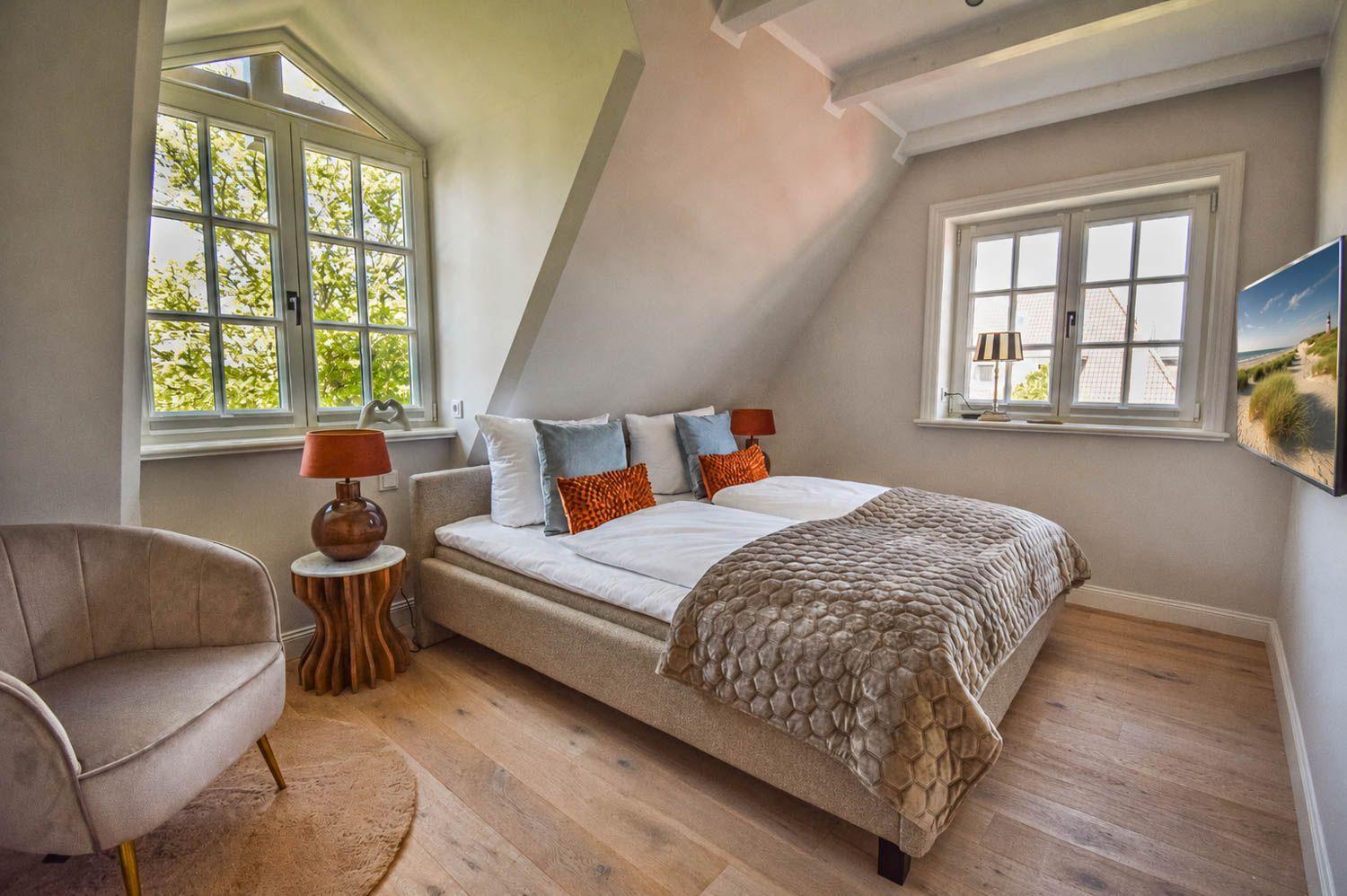 Schlafzimmer mit Doppelbett, zwei Fenstern und Holzboden.