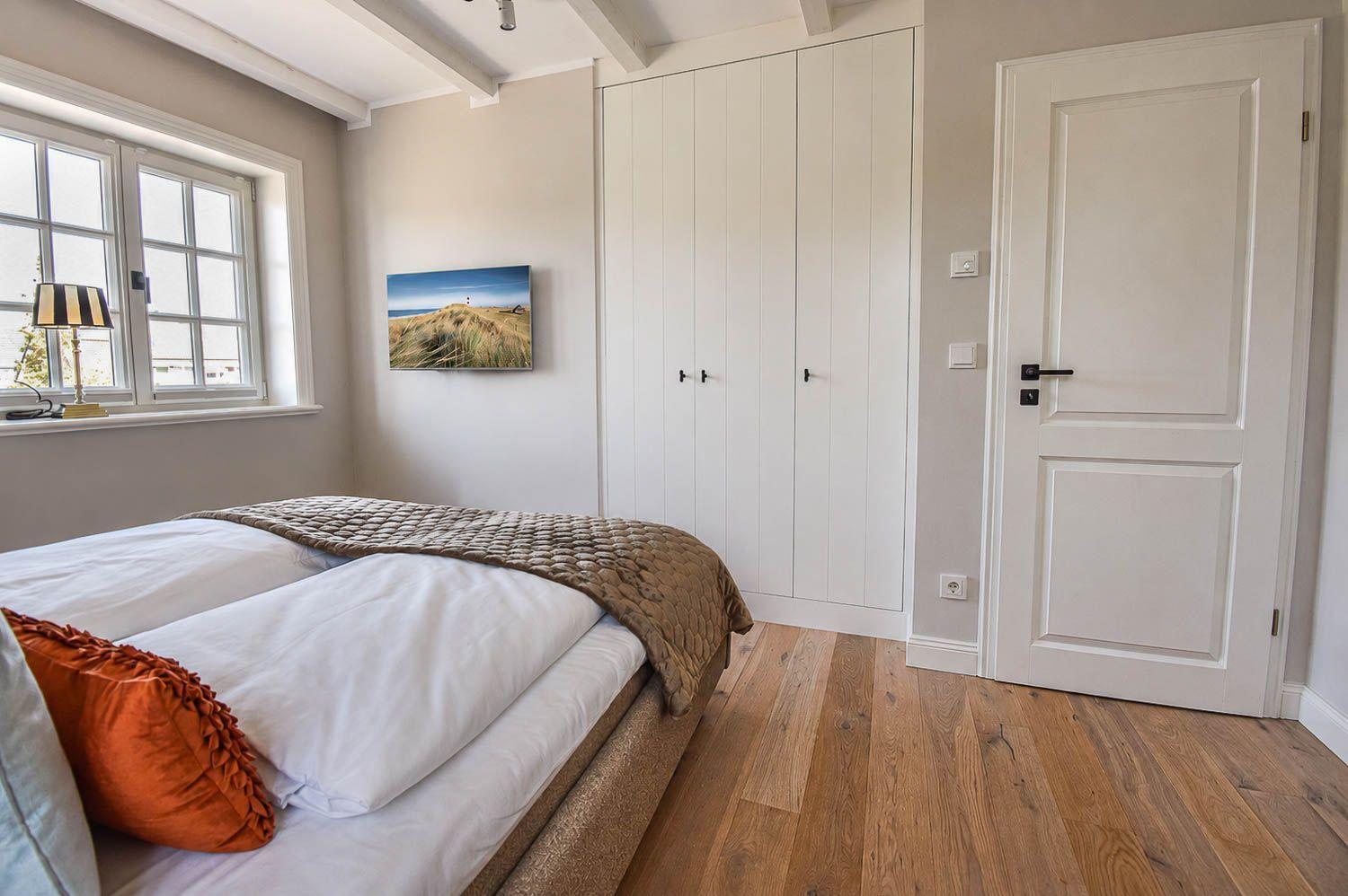 Schlafzimmer mit Bett, Kleiderschrank und Fenster. Holzboden und Wandbild.