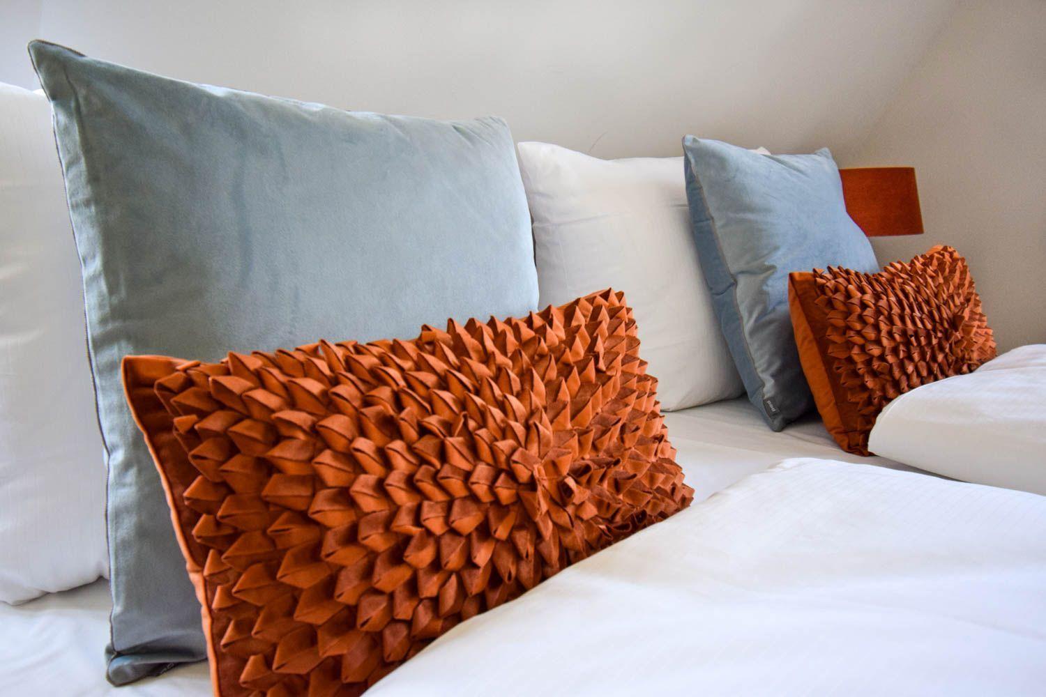 Ein Bett mit weißen Laken und Kissen in Grau und Orange.