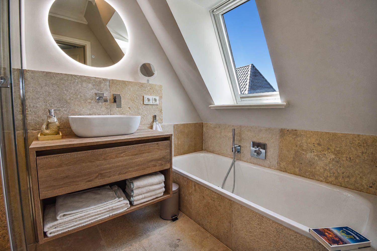 Badezimmer mit Badewanne, Waschtisch und Dusche unter Dachschrägen mit Fenster.