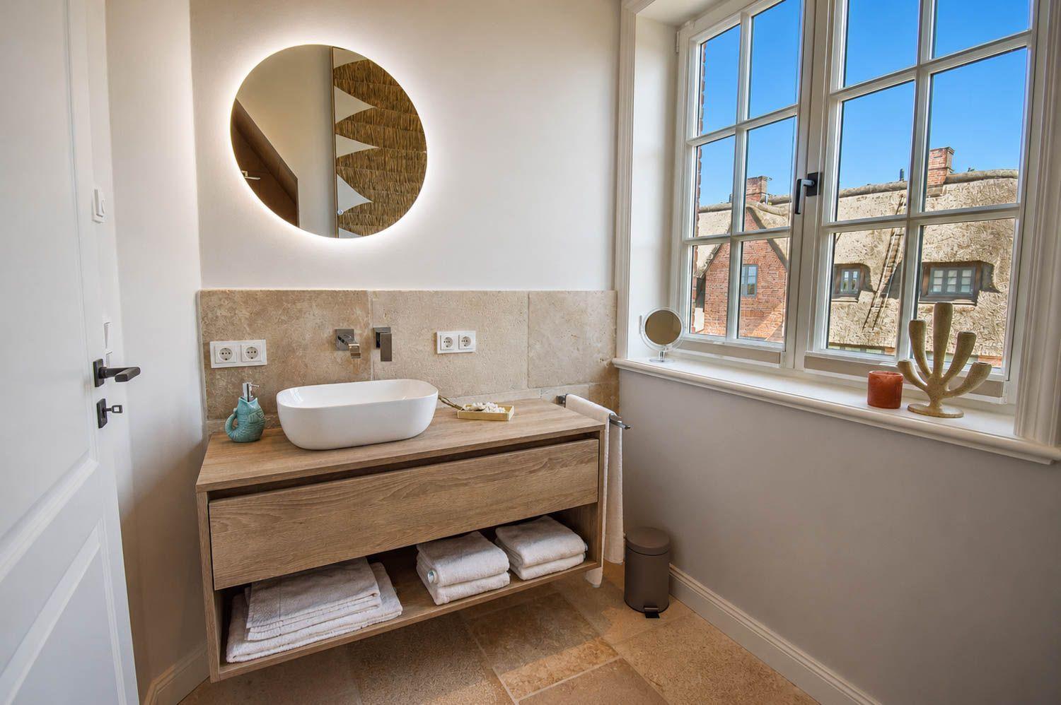 Badezimmer mit Waschtisch, Spiegel und Fensterblick auf Dächer
