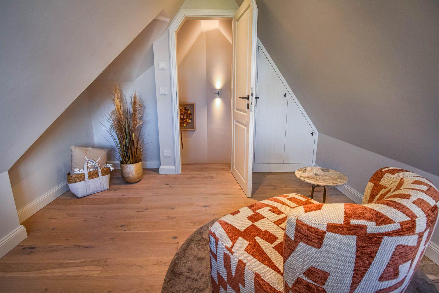 Dachgeschosszimmer mit Sessel, Holzboden und Tür zum Flur.