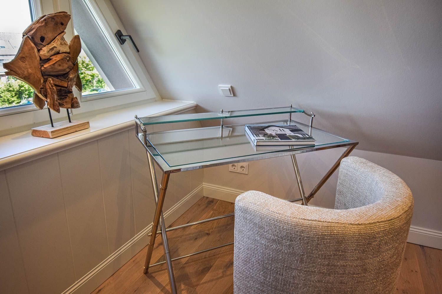 Schreibtisch mit Stuhl unter Dachschräge, Fenster und Holzskulptur