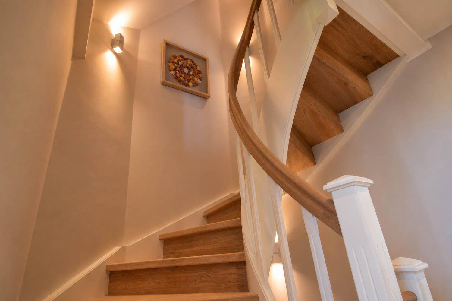 Eine Treppe mit Holzstufen und weißem Geländer führt nach oben. An der Wand hängt ein gerahmtes Kunstwerk.