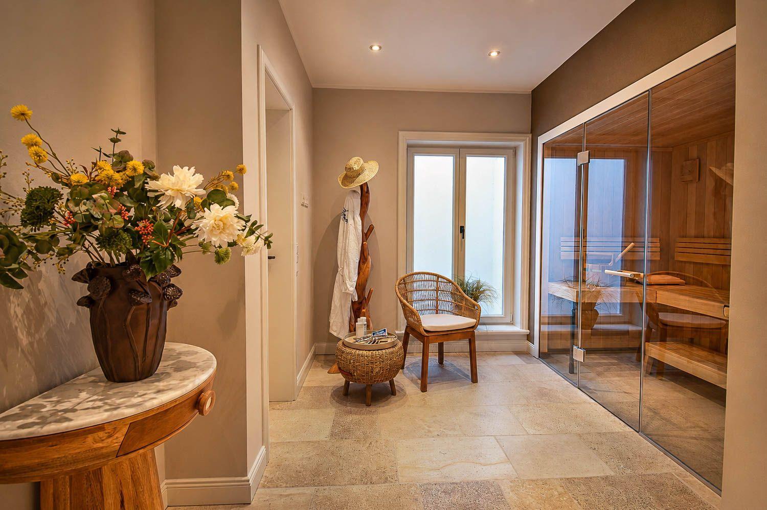 Saunaraum mit Glaswand, Stuhl und Blumenarrangement an der Wand.