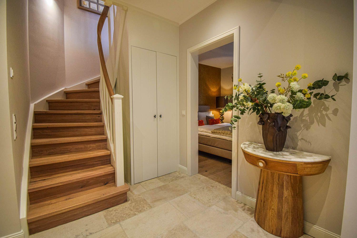 Hausflur mit Holztreppe, Schrank und Blick in Schlafzimmer mit Bett.