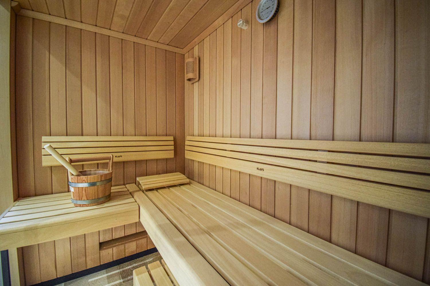 Sauna mit Holzbänken und Holzwand, Holzwaschbecken mit Besen und Thermometer an der Wand.
