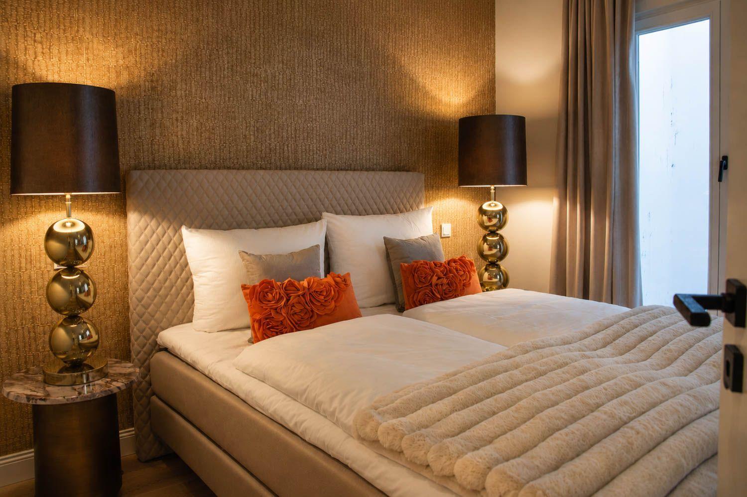 Doppelbett mit Kissen, zwei Nachttische mit Lampen und Fenster mit Vorhängen.
