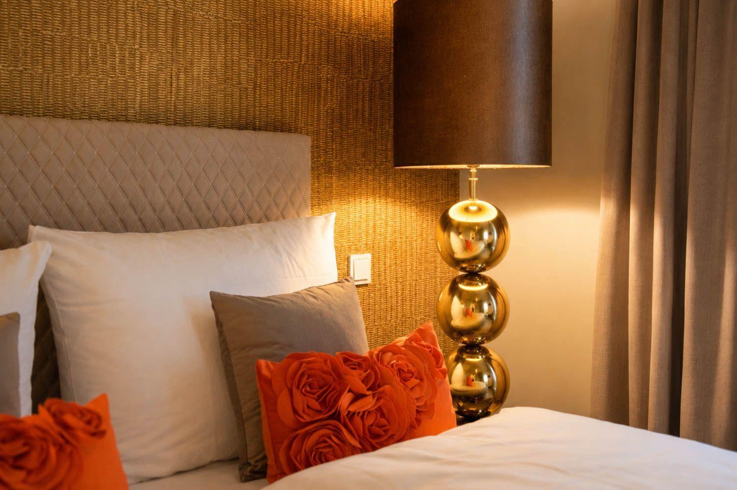 Bettkopfteil mit Kissen und einer Lampe mit goldfarbenen Kugeln.