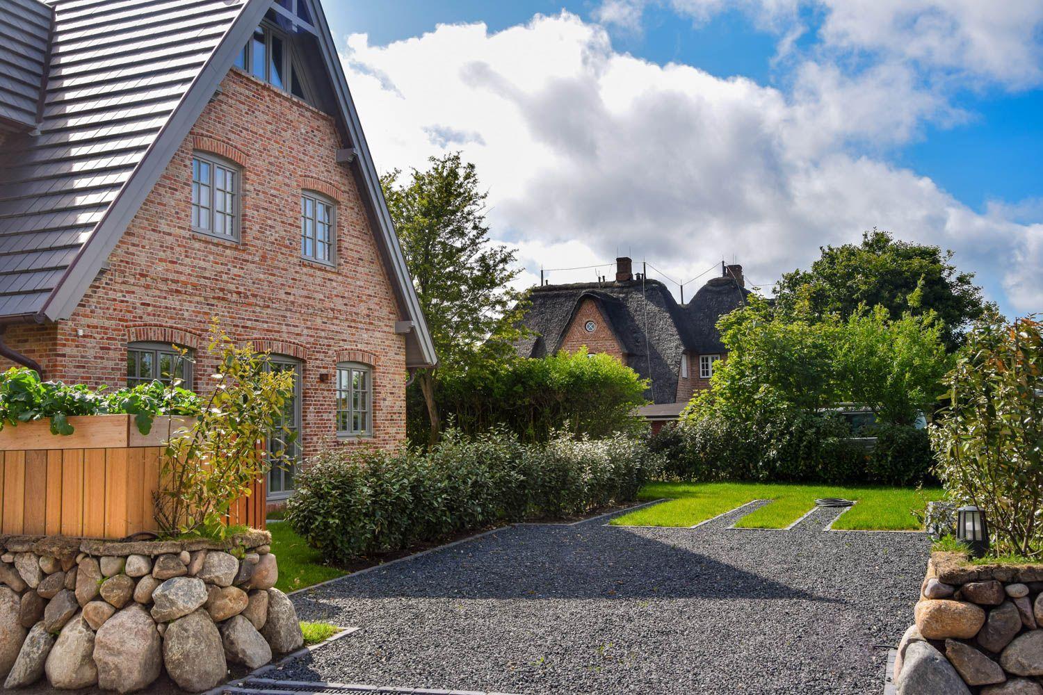 Haus mit Backsteinfassade und Dach aus Schiefer. Gartenweg mit Kies und Steinmauern.