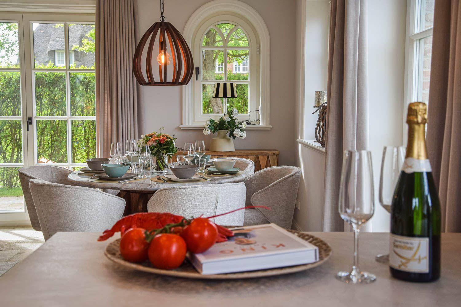 Esstisch mit Stühlen, Flasche Sekt und frischen Tomaten im Esszimmer mit Blick auf Garten.