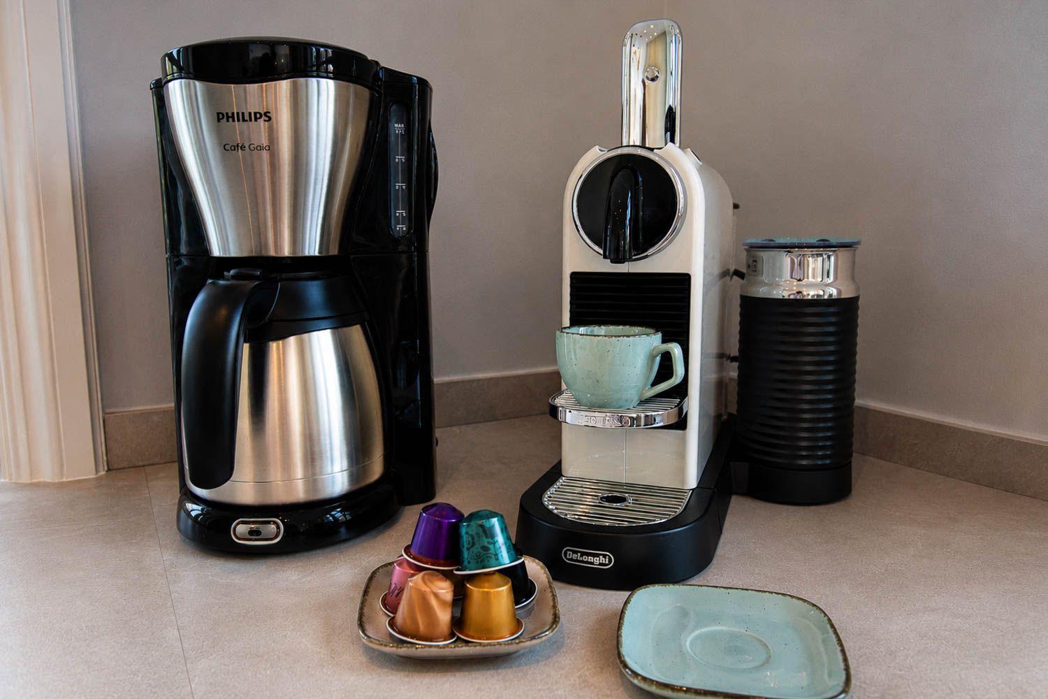 Kaffeemaschine und Nespresso-System mit Tassen und Kapseln auf Arbeitsfläche.