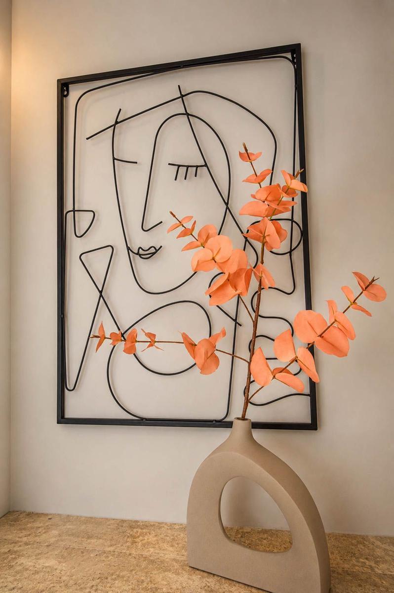 Wanddekoration mit abstraktem Gesicht und orangefarbener Blumenvase auf Marmorplatte.