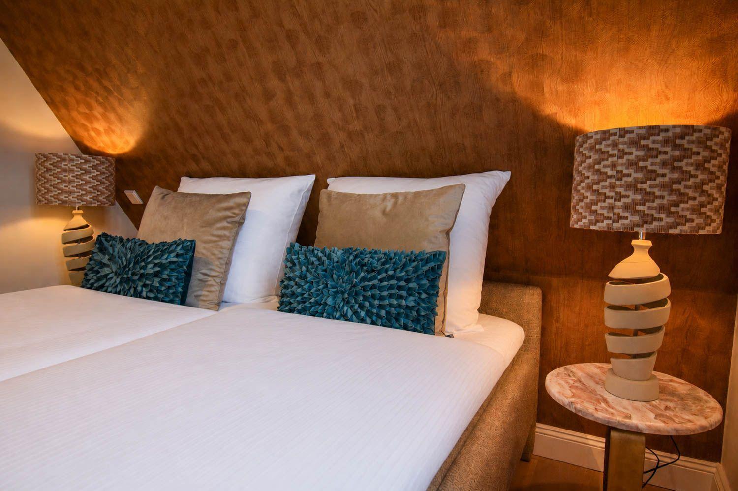 Doppelbett mit Kissen und Nachttischen mit Lampen an der Wand.