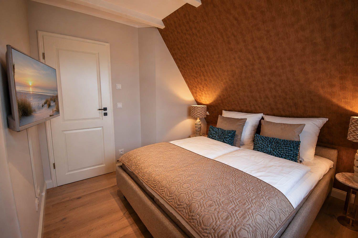 Schlafzimmer mit Bett, Wand-TV und Holzboden. Die Wand hinter dem Bett ist braun gemustert.