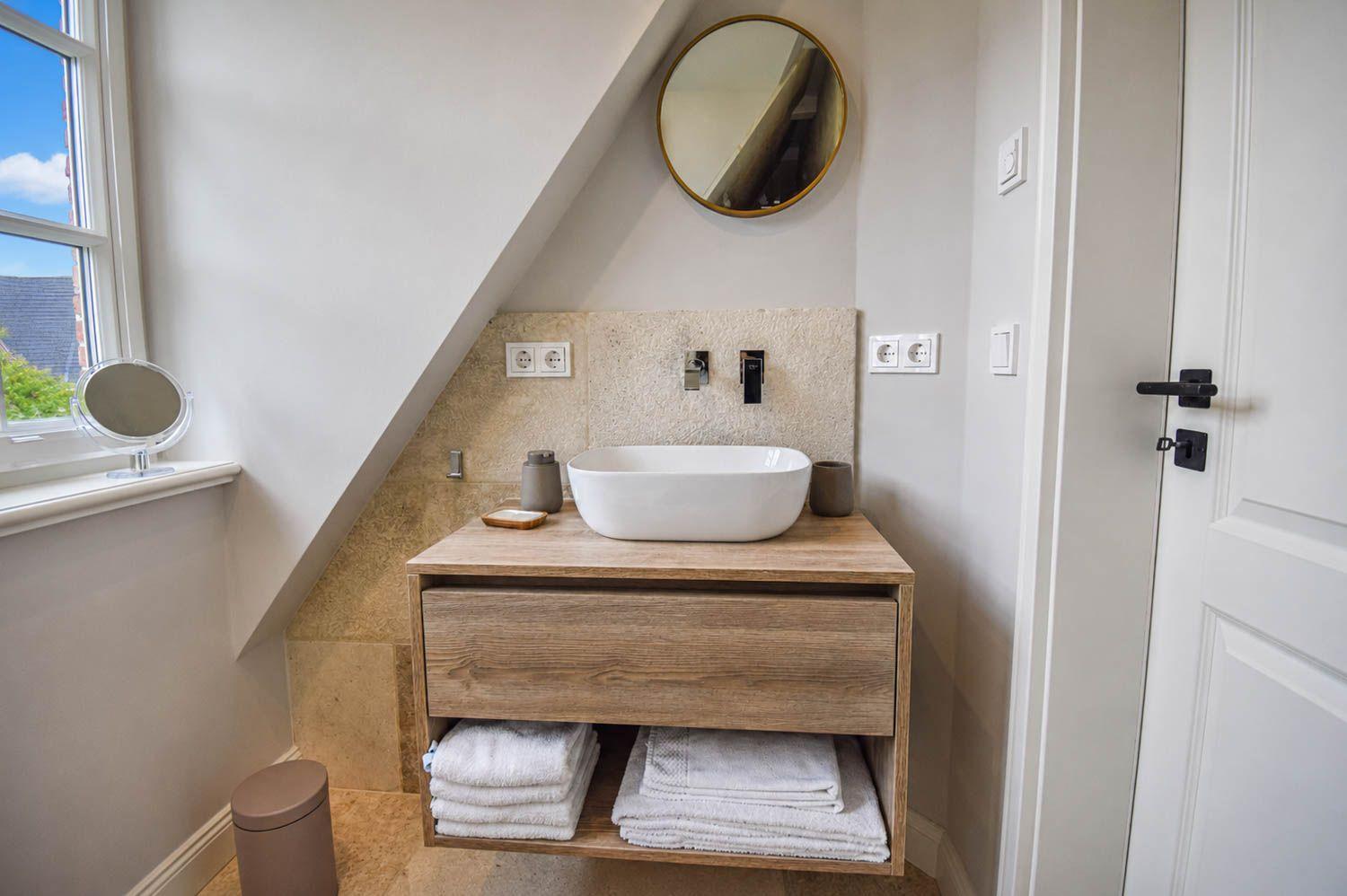 Badezimmer mit Waschtisch, Spiegel und Fenster. Handtücher und Dusche sind vorhanden.