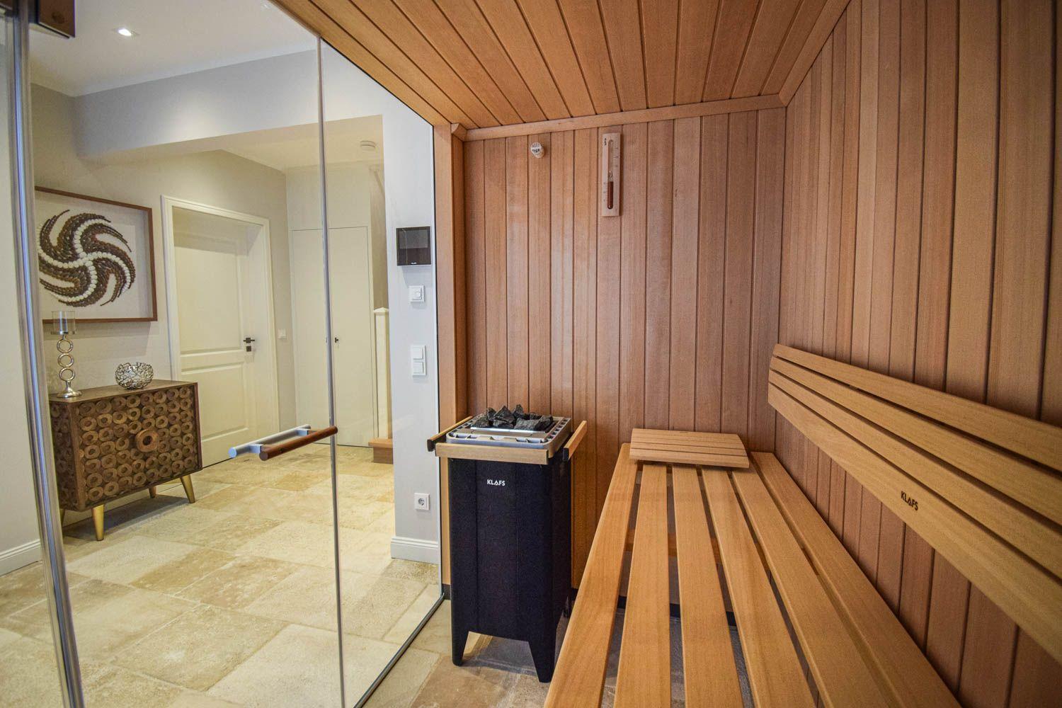 Sauna mit Holzbank und Heizgerät. Durchgehendes Glas trennt den Raum.