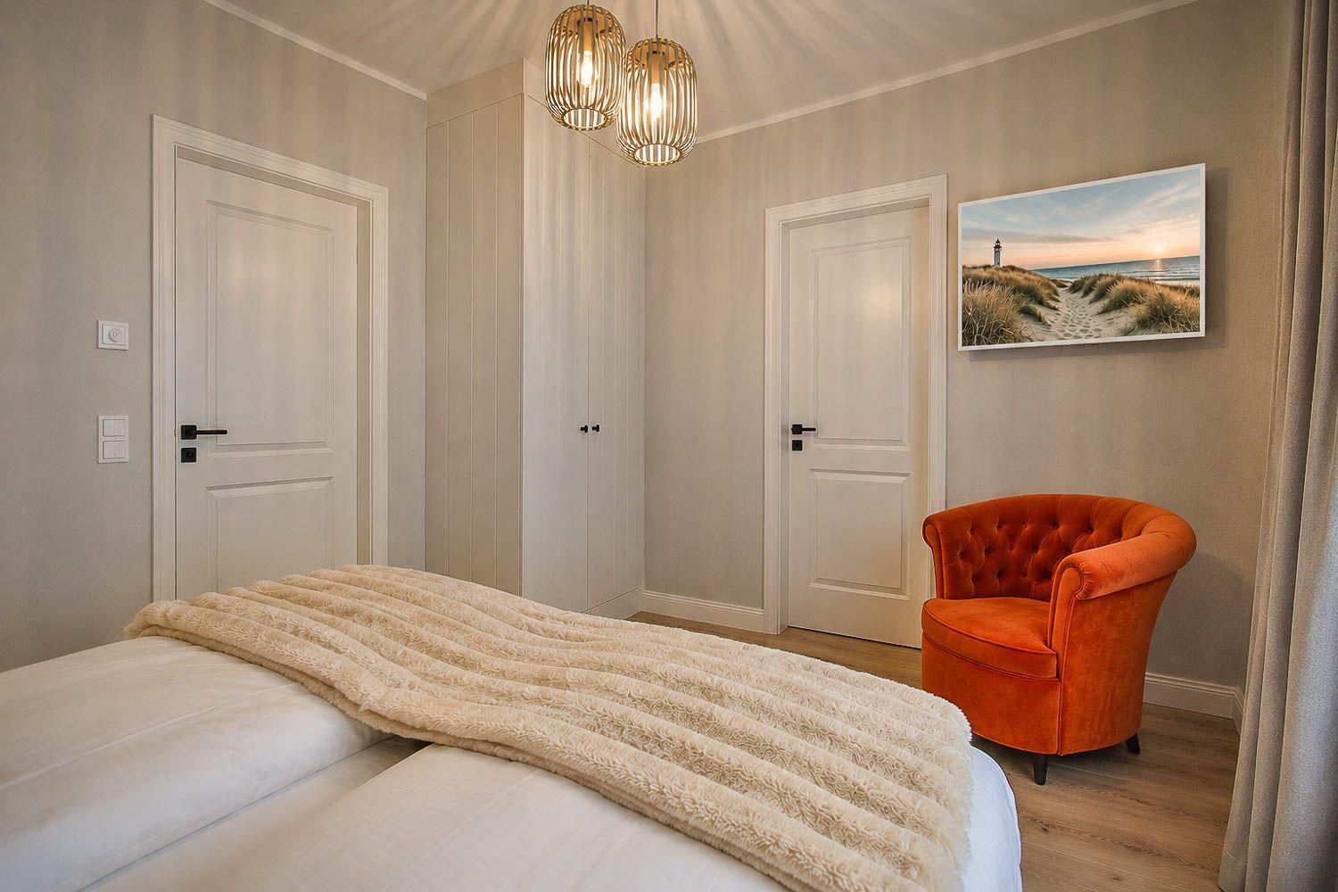 Schlafzimmer mit Bett, orangefarbener Sessel und Wandbild. Deckenleuchte und zwei Türen sichtbar.