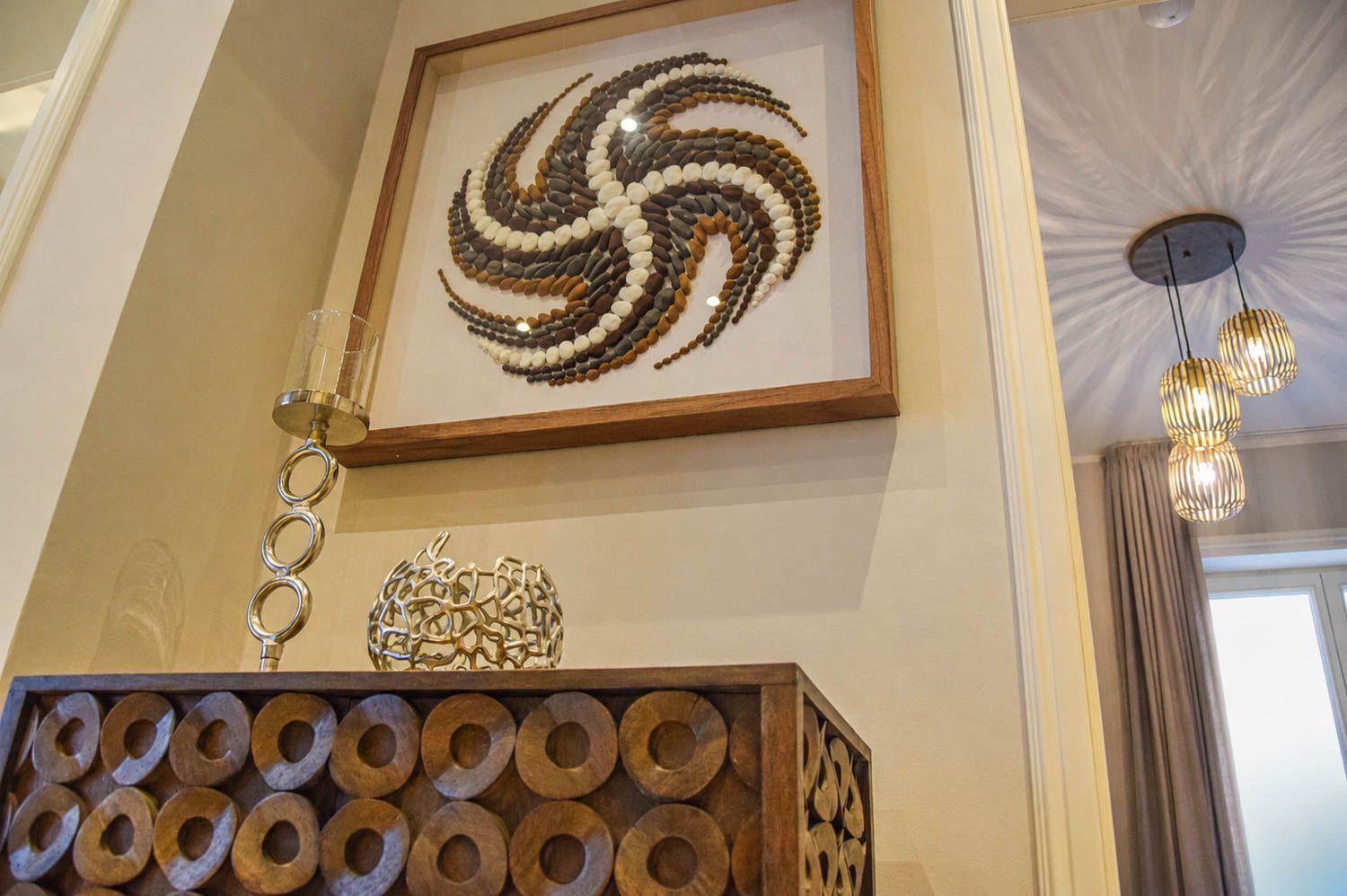 Wandbild aus Steinen über einem Holzschrank mit dekorativen Gegenständen.
