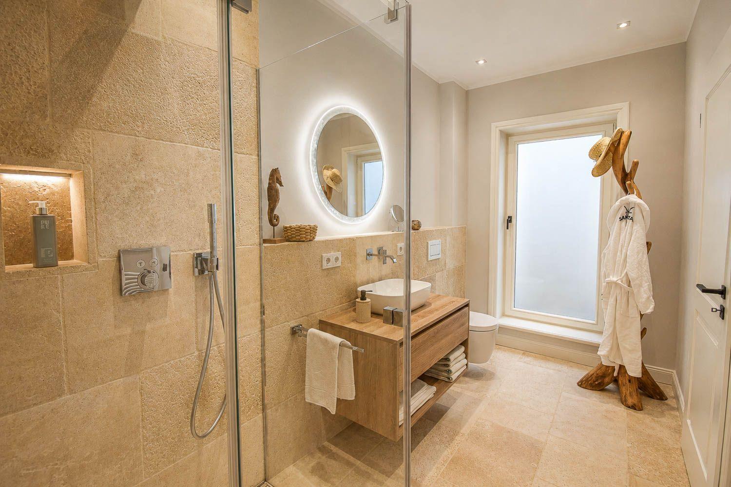Bad mit Dusche, Waschbecken und Fenster. Holzregal, Spiegel und Bademantel.