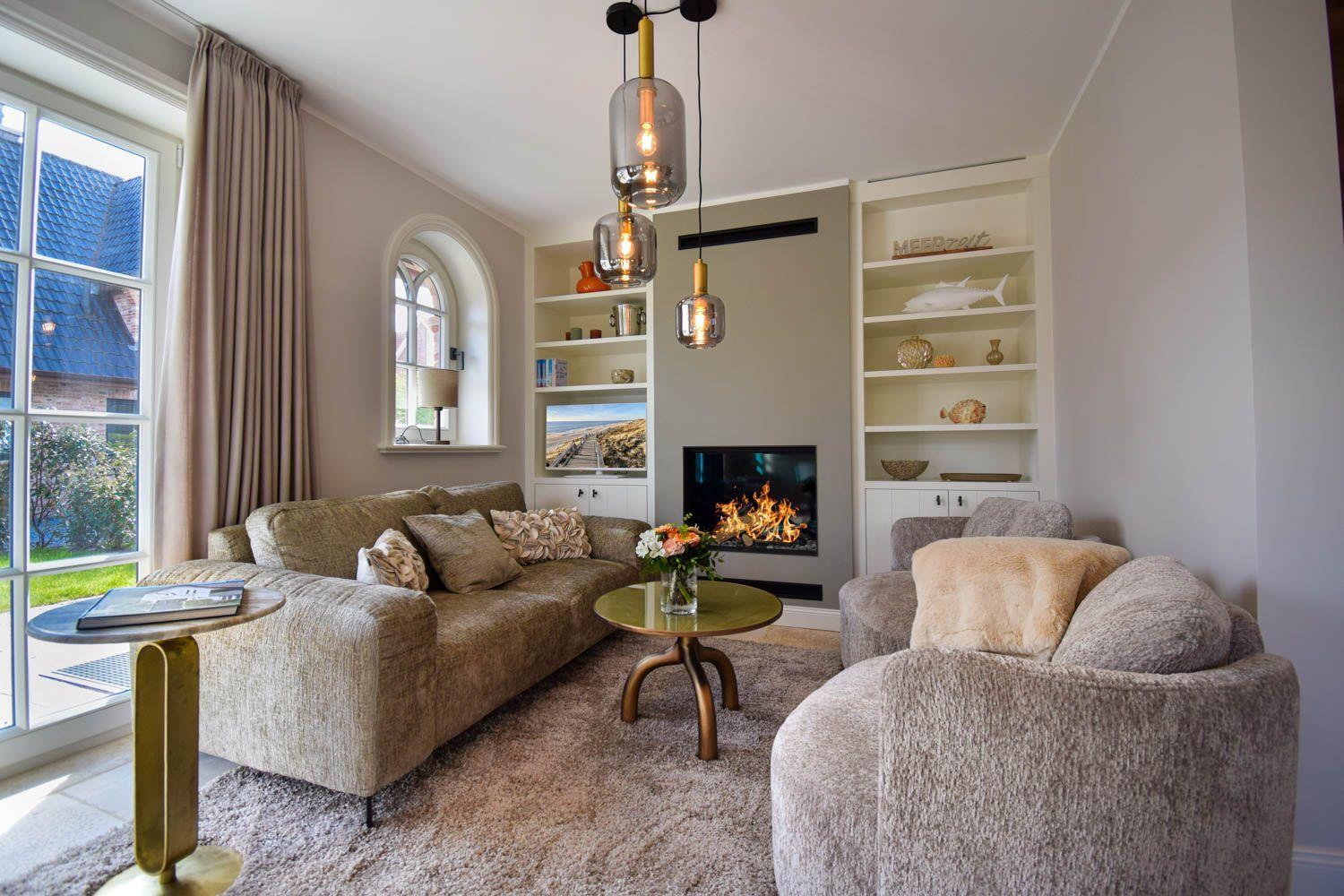 Wohnzimmer mit Sofa, Sessel, Kamin und Bücherregalen.