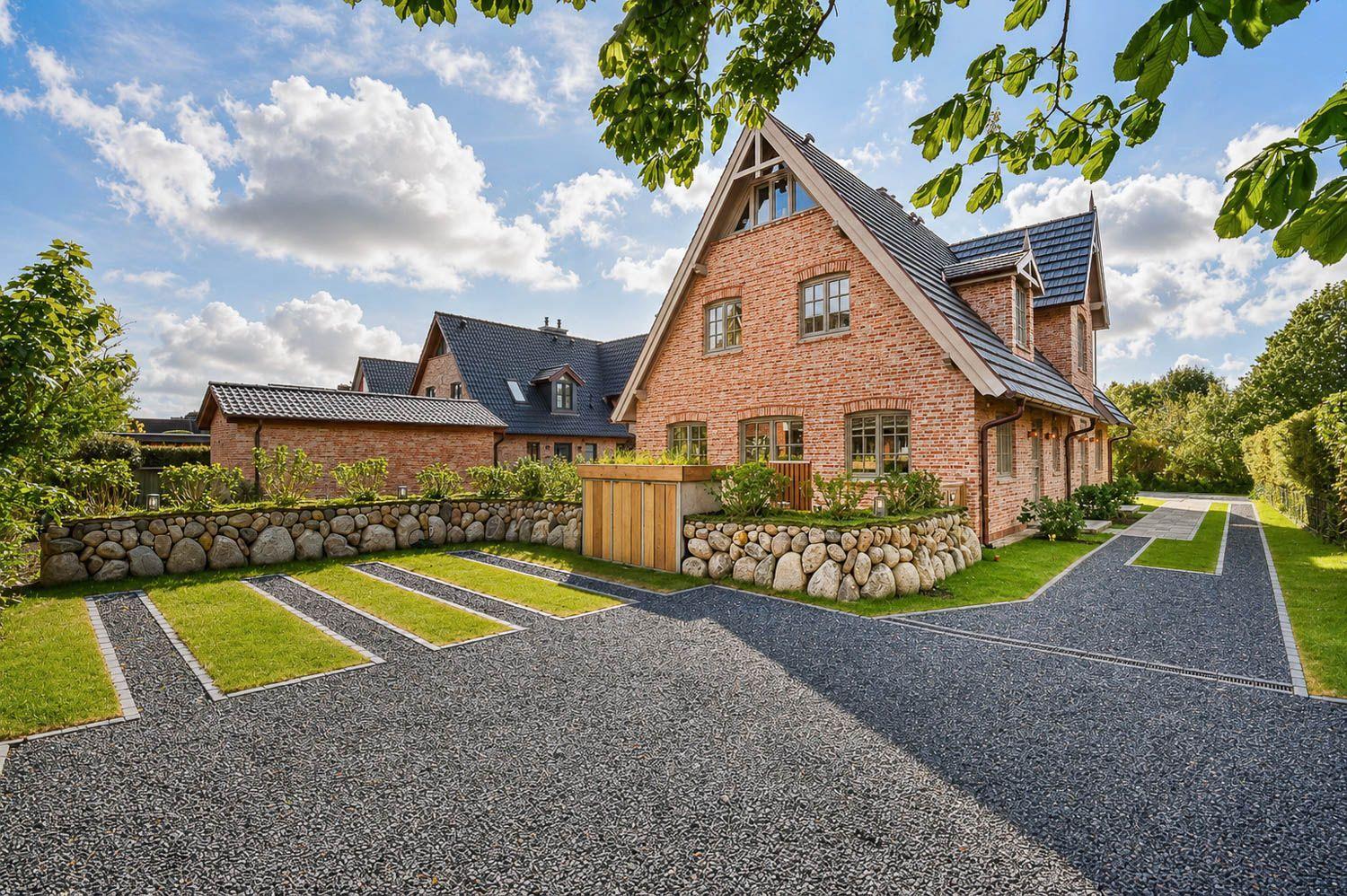 Haus aus Backstein mit Steinmauern und gepflastertem Hof. Grünflächen und Bäume umgeben die Anlage.