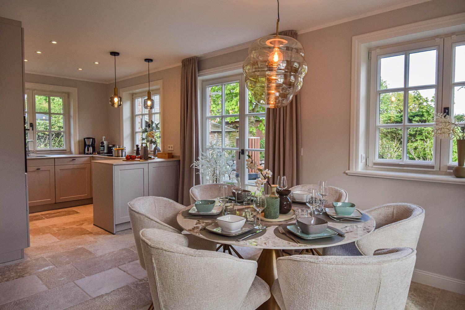 Esszimmer mit runden Tisch und Stühlen, Fenster zur Außenterrasse, Küche im Hintergrund.