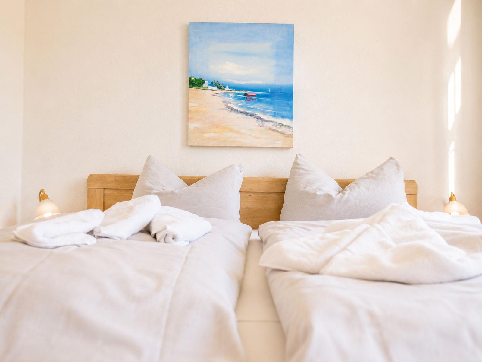 Zwei Betten mit weißen Laken und Kissen. An der Wand hängt ein Strandgemälde.