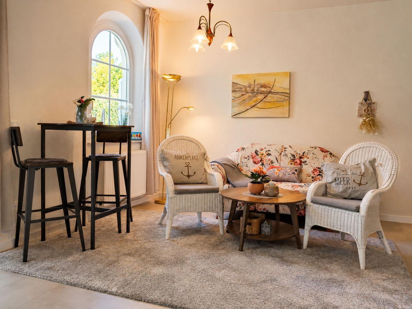 Wohnzimmer mit Sitzgruppe, Tisch, Stühlen und Fenster. Wandbild und Stehleuchte sichtbar.