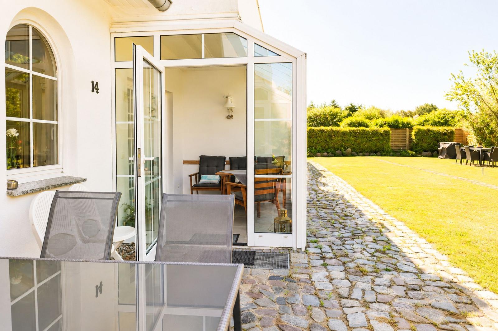 Haus mit Terrasse, Gartentisch und Kiesweg. Durchgehendes Glasdach und grüner Rasen.