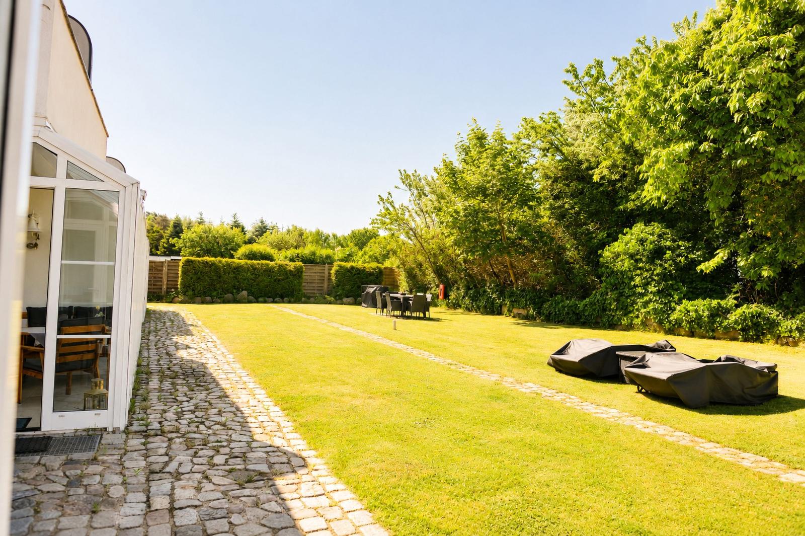 Hinterhof mit Rasen, Steinweg und Gartenmöbeln. Hintergrund: Bäume und Hecke.