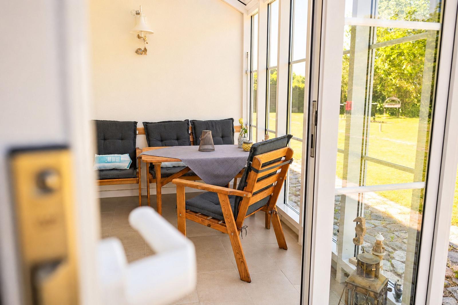 Terrasse mit Holztisch, Stühlen und Sitzbank. Durchgehende Glasfront zum Garten.