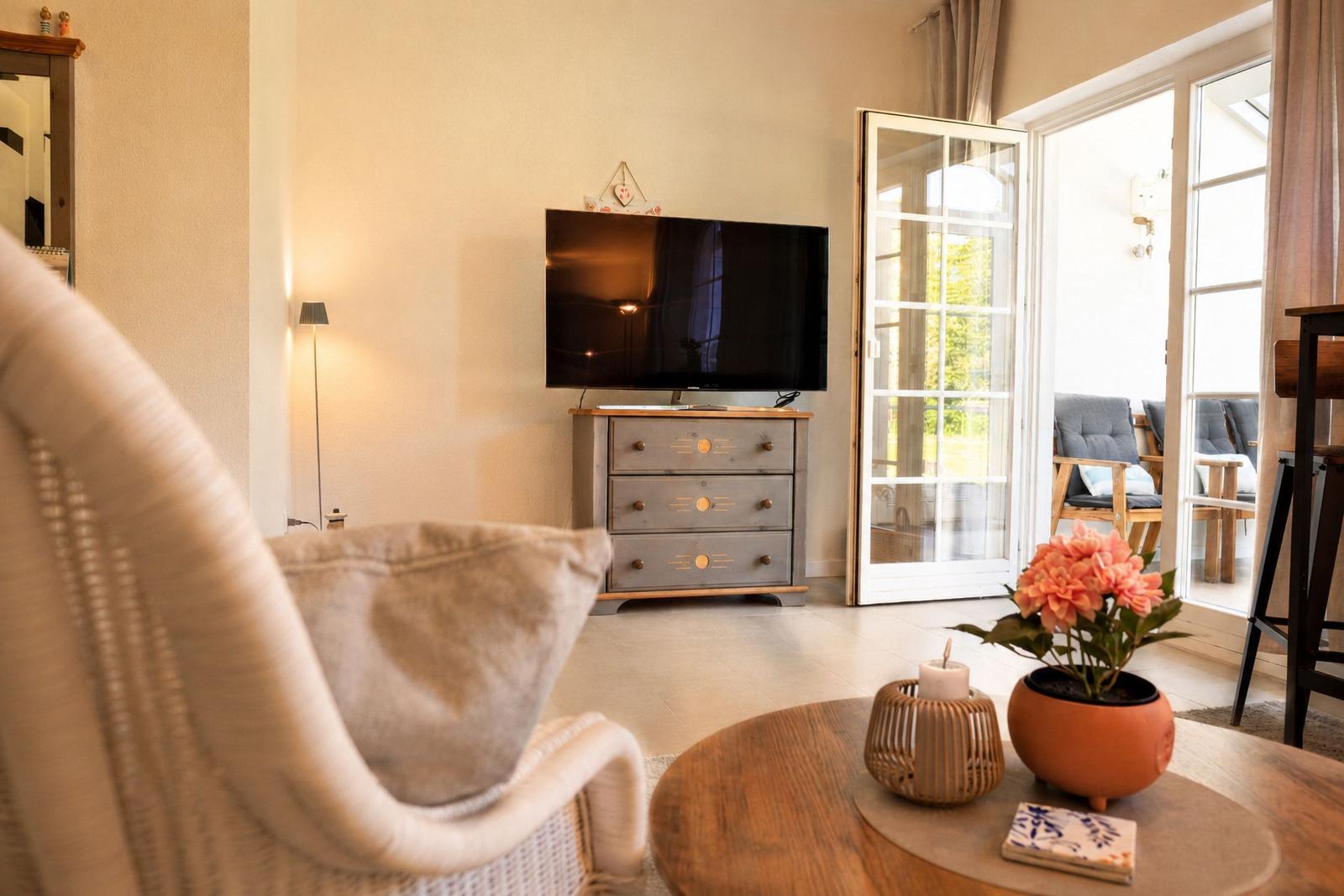 Wohnzimmer mit Fernseher, Schrank und Terrassentür. Tisch mit Blumen und Kerze.