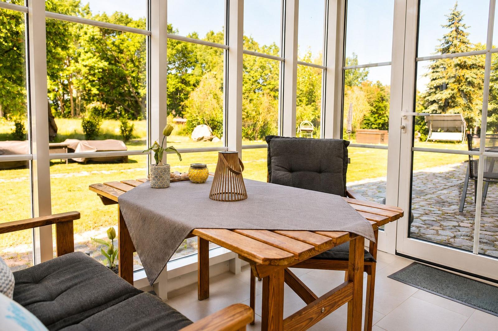 Holztisch mit Tischdecke und Stühlen vor großem Fenster mit Blick auf Garten.