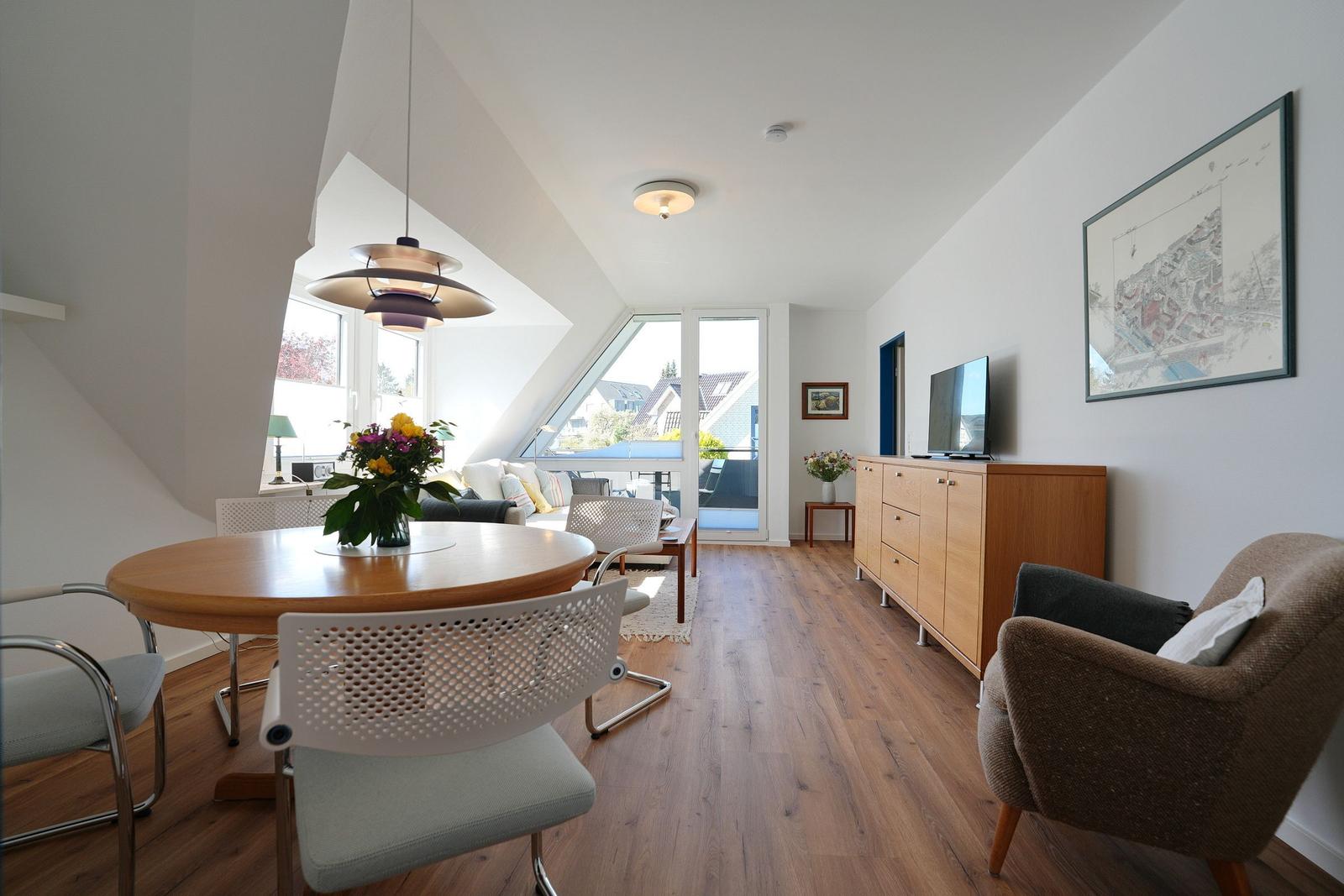 Wohn- und Essbereich mit Holzboden, TV-Schrank und Schlafbereich mit Blick auf Balkon.