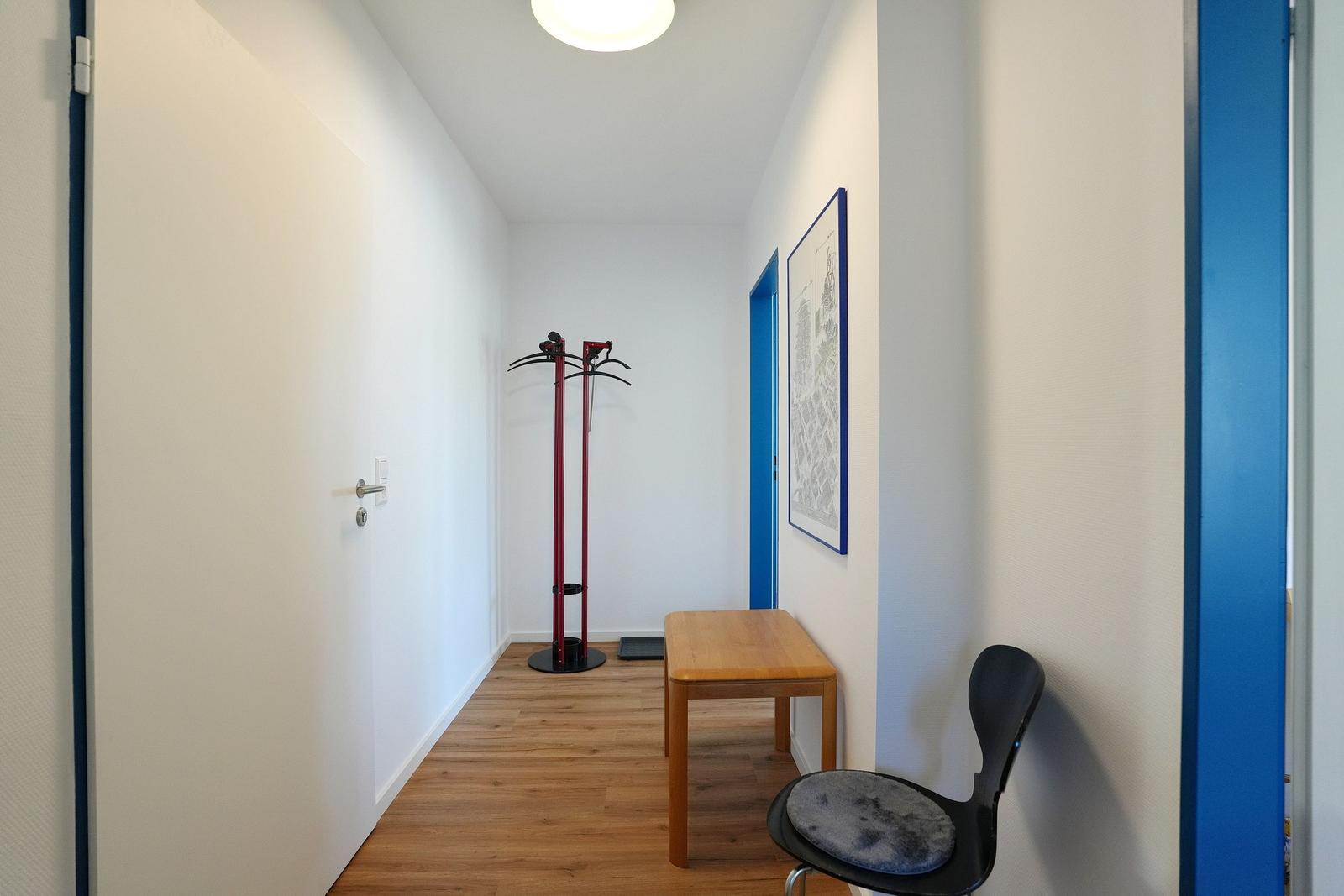 Flur mit Holzboden, Stuhl, Tisch und Kleiderständer.