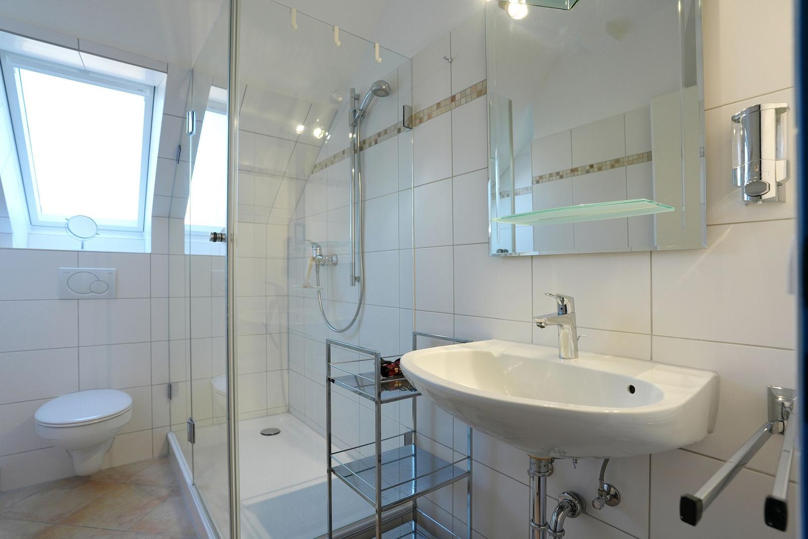 Badezimmer mit Dusche, Waschbecken und Toilette. Fenster sorgt für Tageslicht.